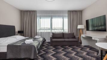 Hotelkamer met een bed, een slaapbank, een bureau, een televisie en een raam met gordijnen.