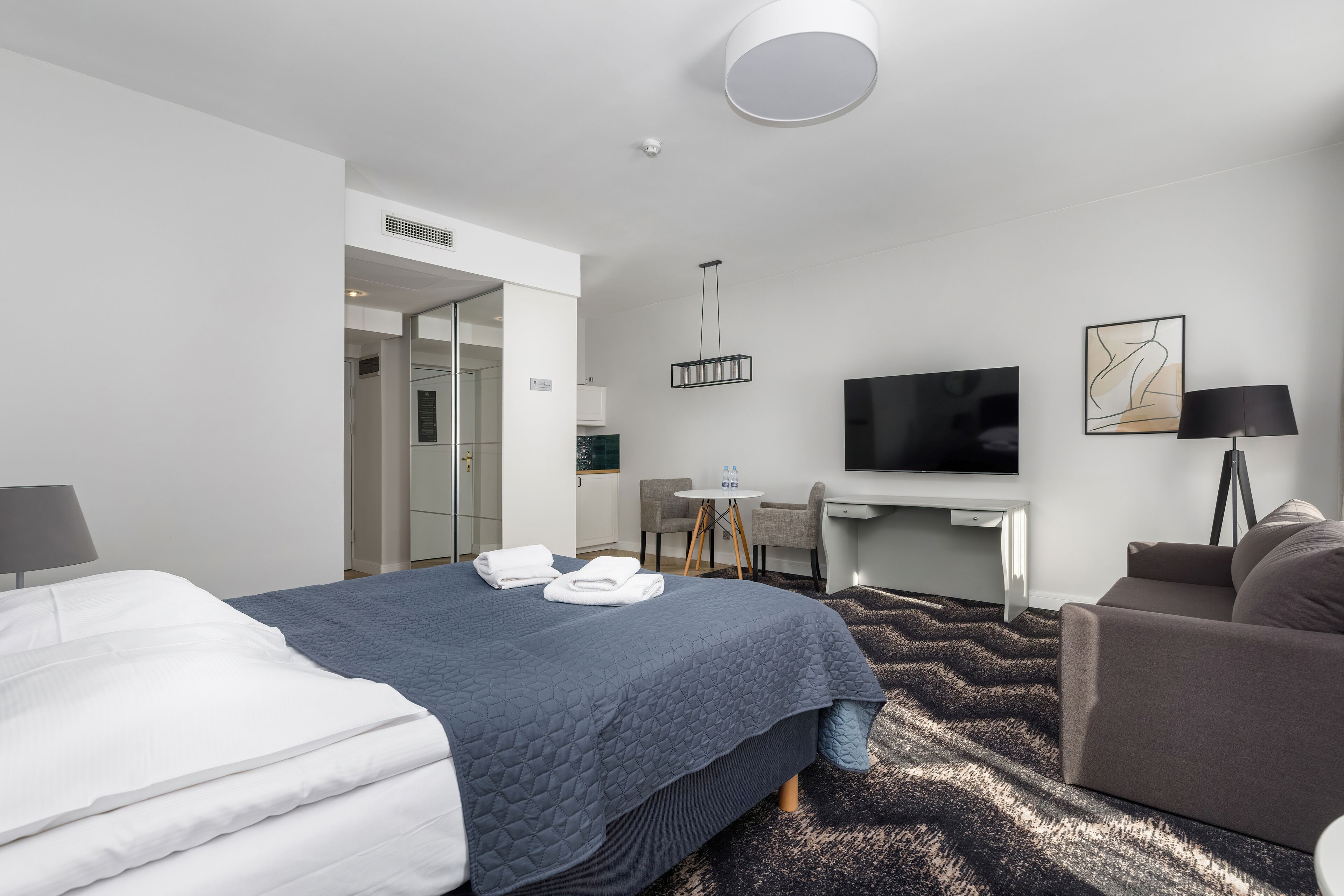 A modern hotel room with a large bed, a desk, a television, and a sofa.