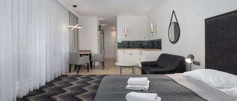A modern hotel room with a large bed, a desk, a chair, a round table, and a dark-colored headboard.