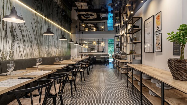 L’intérieur d’un restaurant avec de longues tables, des chaises noires, des luminaires suspendus et un sol à motifs.