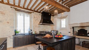 Une cuisine avec des meubles en bois foncé, un grand îlot central doté de tabourets, un mur en pierre et un plafond rustique.