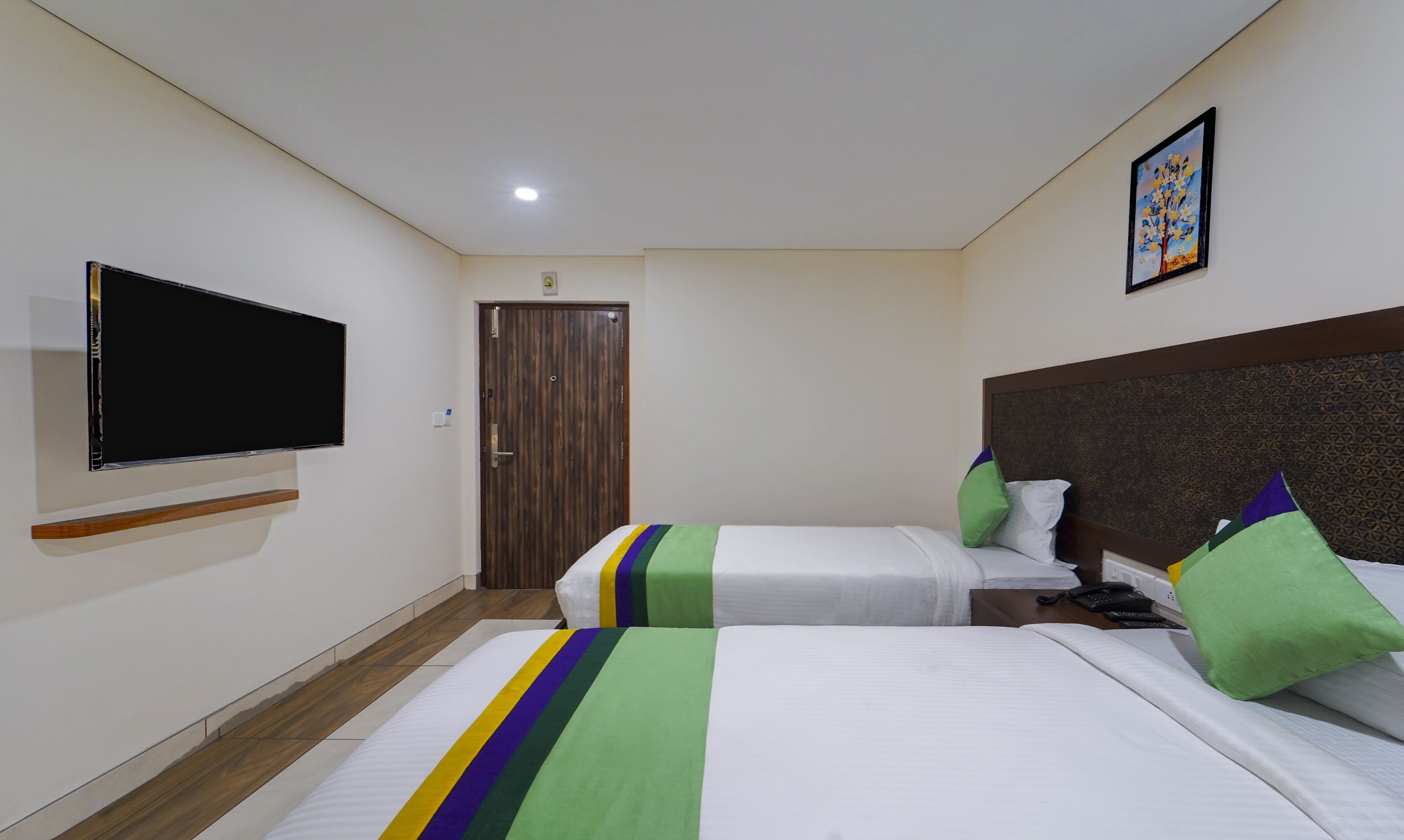 A hotel room with two beds, a TV, a door, and a painting on the wall.