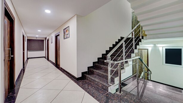 A modern hotel hallway with a marble floor, wooden doors, and a staircase with metal railings. - Treebo Era City Stay (Chennai)