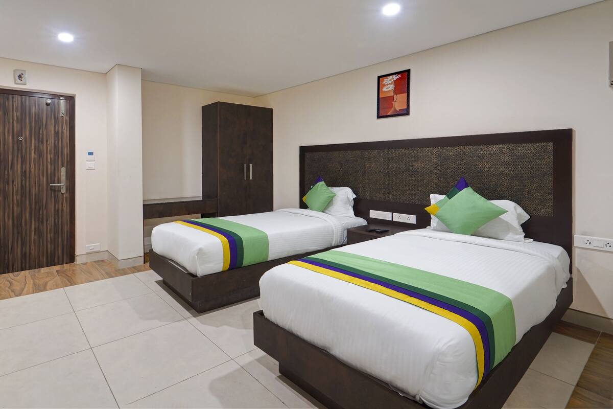 Habitación de hotel con dos camas, un armario de madera, un cuadro en la pared y suelo de baldosas.