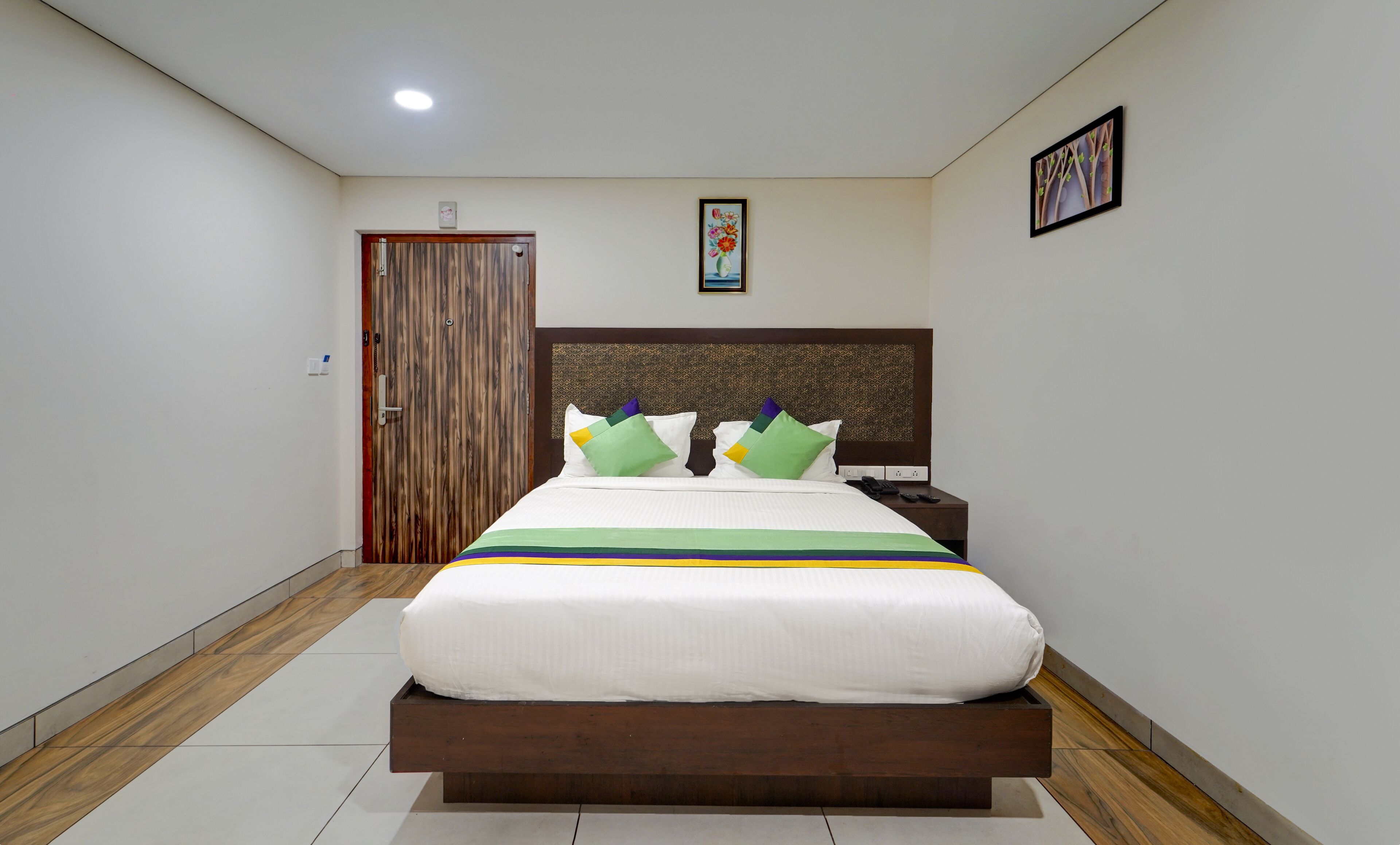 A neatly arranged hotel room with a wooden bed frame, a nightstand, and a wall-mounted telephone.