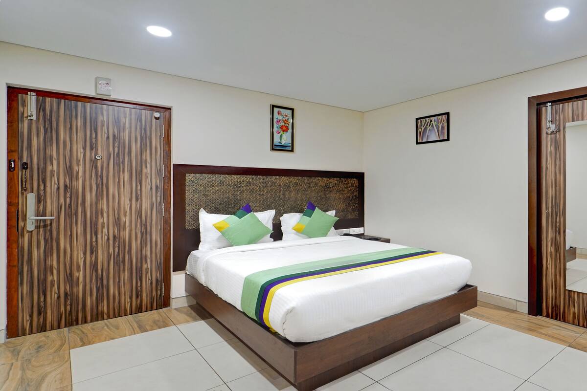 Un dormitorio ordenado con cabecera de madera, cama con ropa de cama blanca y almohadas coloridas, y dos cuadros en la pared.