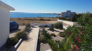 Une vue sur la côte, avec un ciel dégagé, une voiture garée et un bâtiment doté d’un balcon donnant sur la mer.