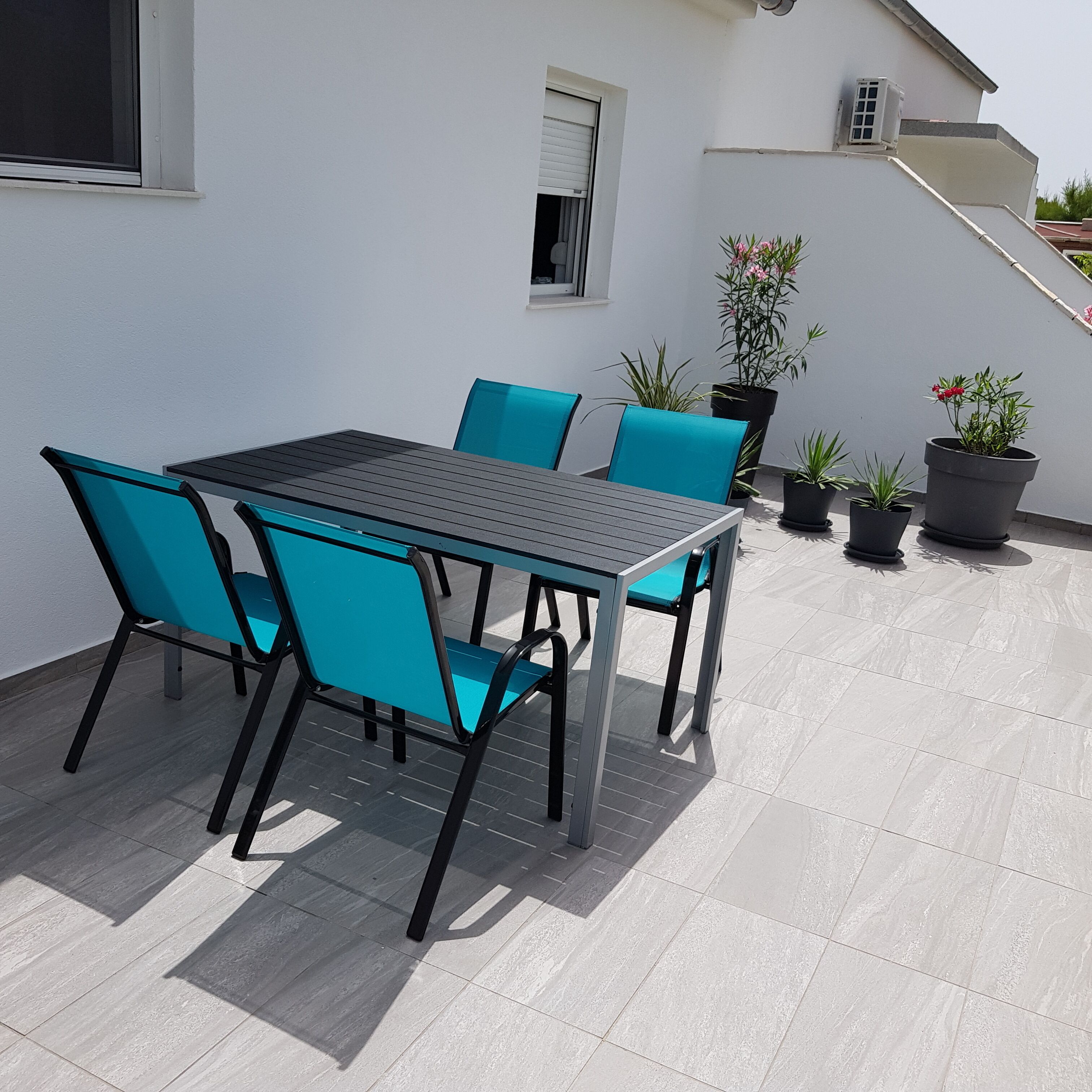 Une terrasse avec une table et des chaises, des plantes en pot et un escalier.