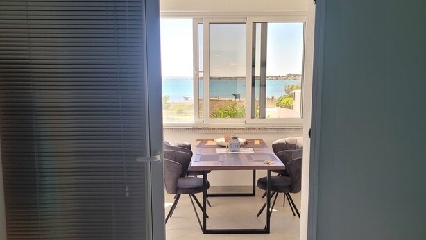 Une chambre avec un lit, une table entourée de chaises et une vue sur la mer grâce à de grandes fenêtres.