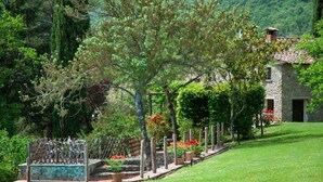 A stone building with a tiled roof, surrounded by a well-maintained garden with various plants and flowers. - Villa con Piscina - Casale Rancaccio (Arezzo)