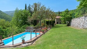 A swimming pool with a stone border, a stone wall, and a grassy lawn.