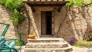 A stone building with a wooden door, a small porch with steps, and a potted plant. - Villa con Piscina - Casale Rancaccio (Arezzo)