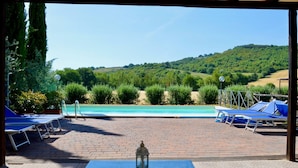 A pool area with blue lounge chairs, a brick patio, and a view of a hill with trees. - Villa con Piscina - Villa Chiara (Marsciano)