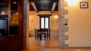 A dining area with a brick column, wooden chairs, a table, and a television on a cabinet. - Villa con Piscina - Villa Chiara (Marsciano)