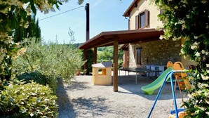 A covered outdoor area with a table and chairs, a play structure, and a stone building in the background. - Villa con Piscina - Villa Chiara (Marsciano)