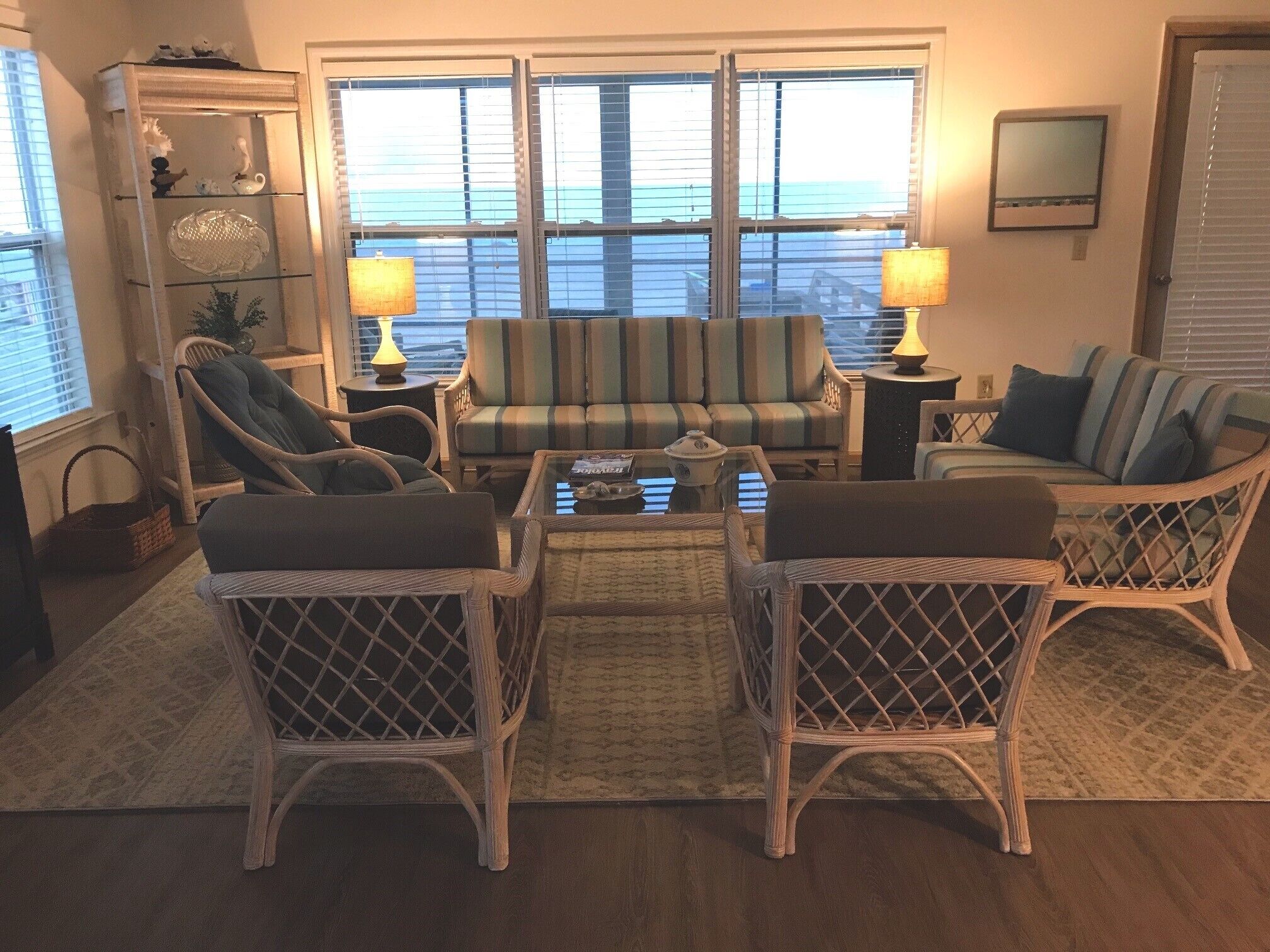 Ein Wohnzimmer mit Korbmöbeln, einem gestreiften Sofa und Blick auf das Meer durch große Fenster.