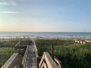 A wooden boardwalk leading to a beach with grassy dunes and a clear view of the ocean.
