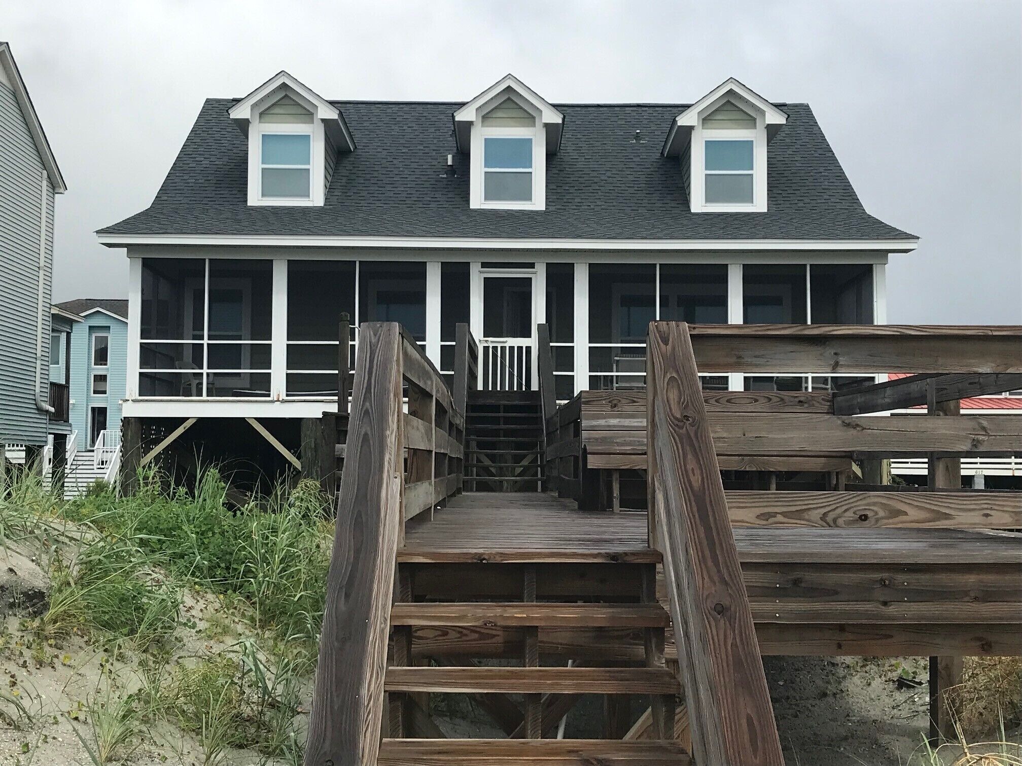 A wooden staircase leading to a house with a dark roof and white trim.