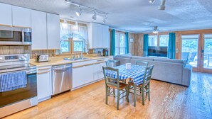 A modern kitchen with stainless steel appliances, a dining area with a checkered tablecloth, and a cozy seating area with a TV. - Jo Jo's House - Off-Ocean, Dog Friendly (Pawleys Island)