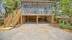 A two-story wooden cabin with a balcony, a wooden staircase, and a gravel driveway. - Jo Jo's House - Off-Ocean, Dog Friendly (Pawleys Island)