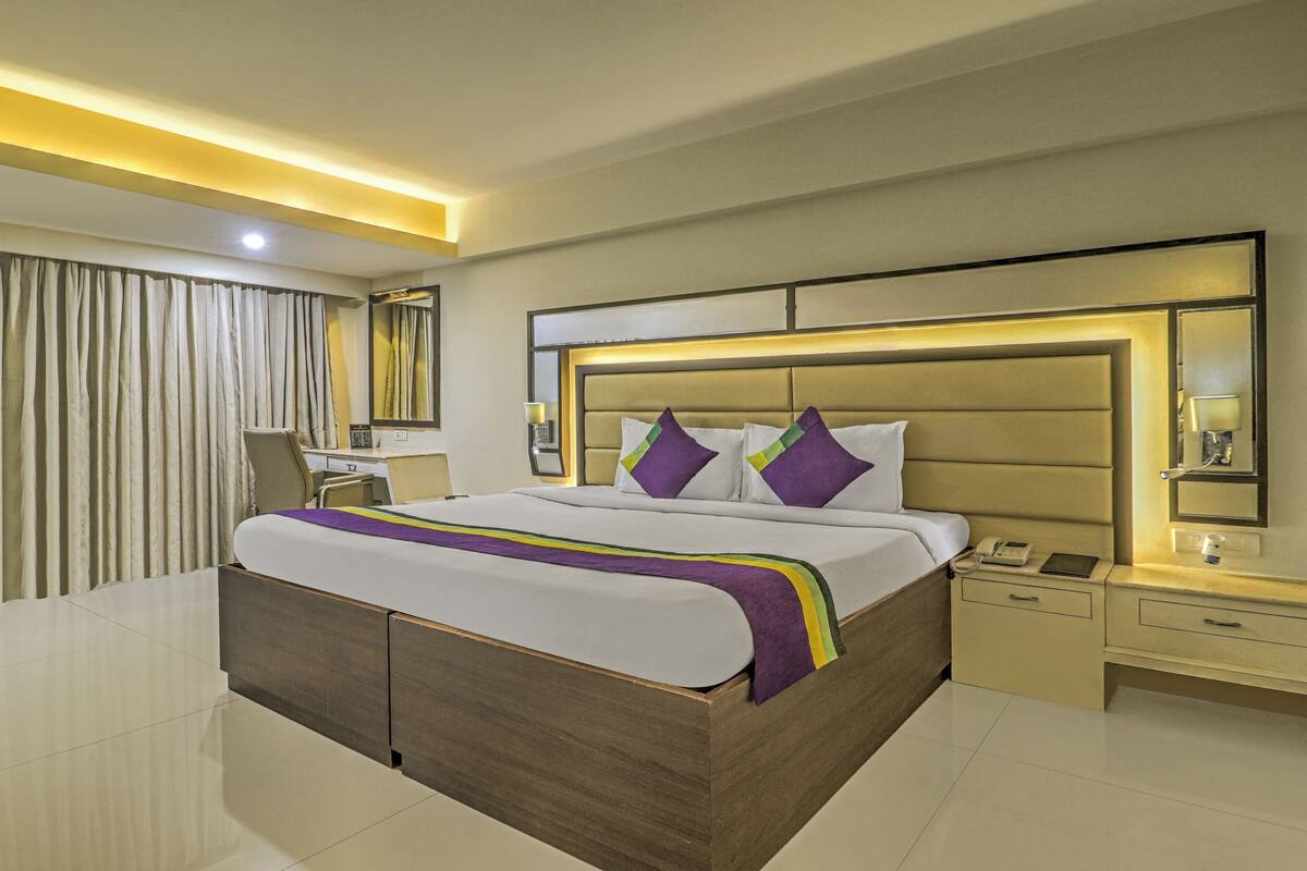 A modern hotel room with a large bed, bedside tables, a desk, and a mirror.