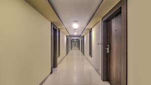 Un long couloir étroit, avec des portes de chaque côté, un sol carrelé et un plafond doté d’un éclairage encastré.