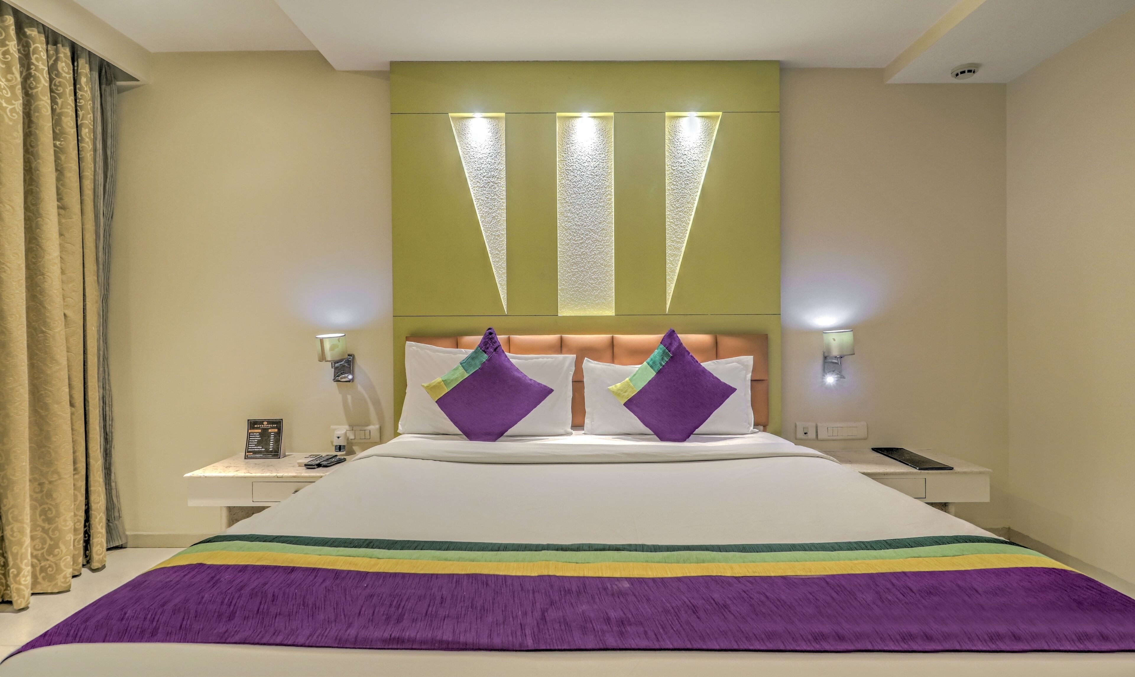 Habitación de hotel con una cama grande, dos mesitas de noche, cabecero con iluminación integrada y vistas a la ciudad.