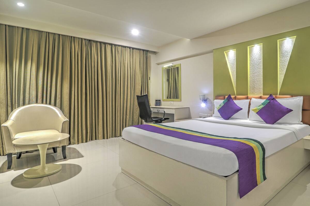 A hotel room with a bed, a desk, a chair, and a large window with curtains.