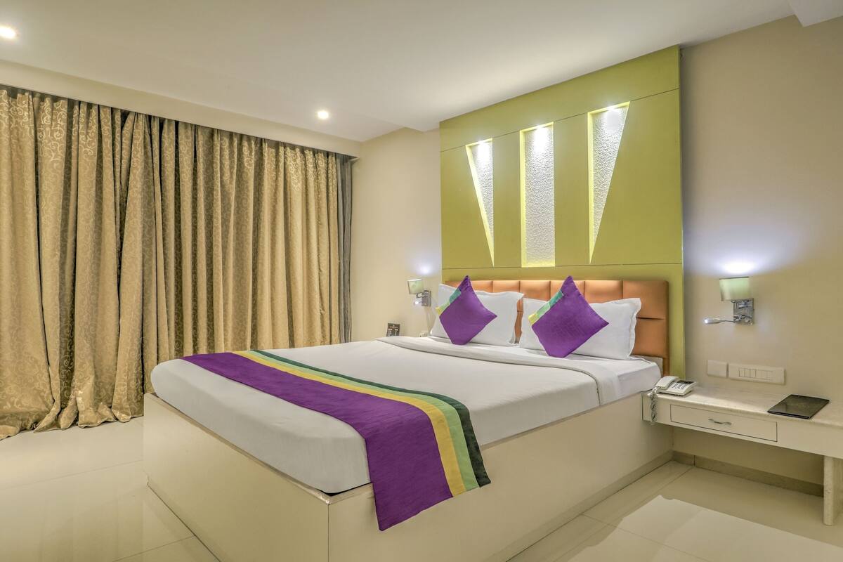 A hotel room with a large bed, a bedside table, and a window with curtains.