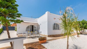 A white building with a patio area, a wooden deck, and a small palm tree. - Villa Amanecer - Plus (Calpe)