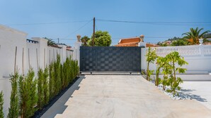 A gated entrance with a checkered gate, a concrete pathway, and a row of green plants on either side. - Villa Amanecer - Plus (Calpe)