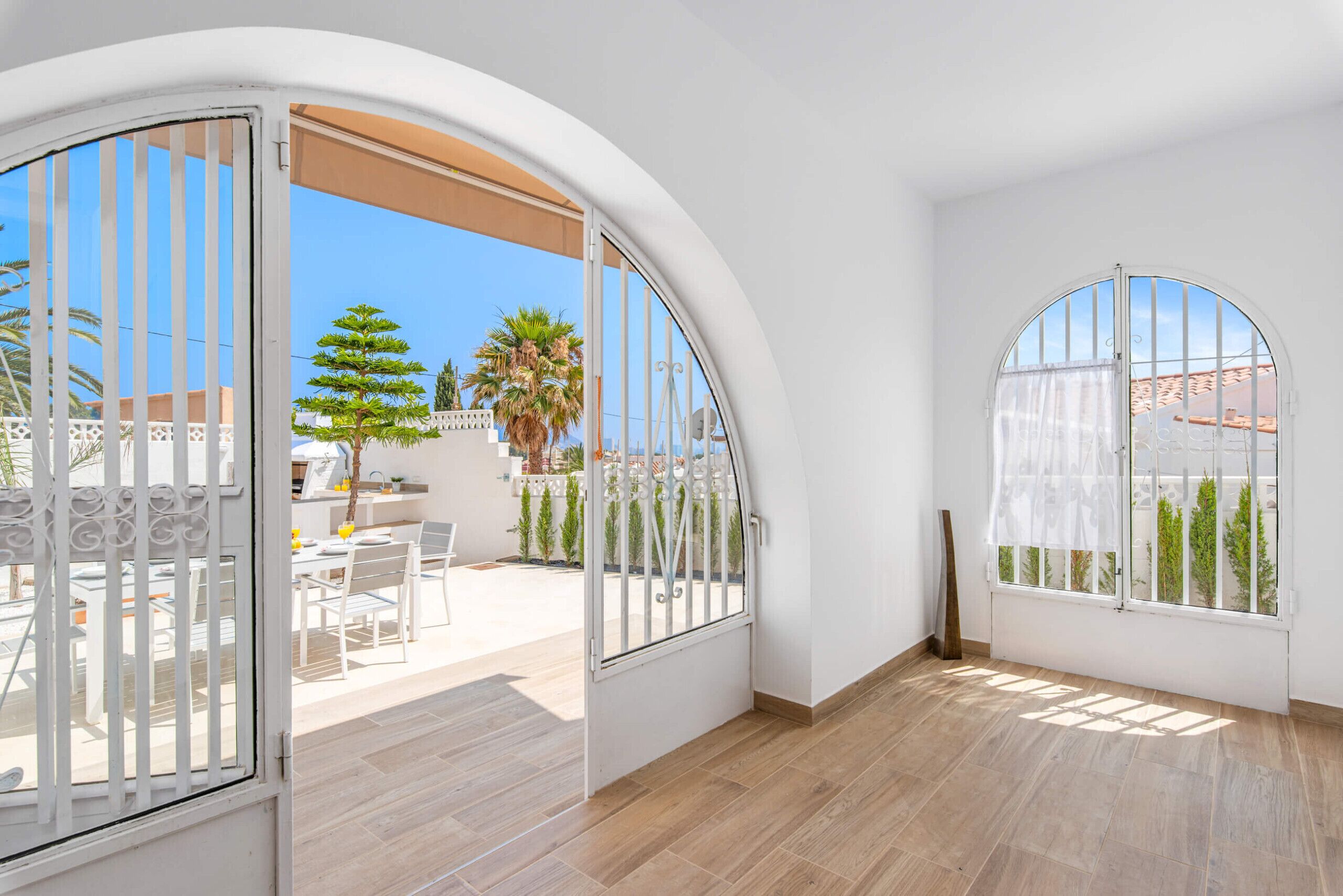 A room with arched windows, a patio with outdoor furniture, and a view of palm trees and buildings.