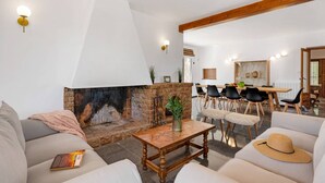 Sala de estar com lareira, área de jantar com cadeiras e um sofá com chapéu.