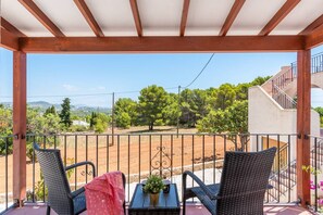 A balcony with wicker chairs, a small table with a plant, and a view of a rural landscape. - Villa Estacion - PlusHolidays (Calpe)