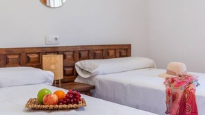 Quarto de hotel com duas camas, mesa de cabeceira com cesta de frutas e espelho fixado na parede.