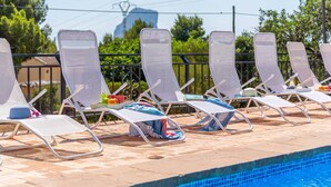 Uma área na beira da piscina com espreguiçadeiras dispostas em fileiras, um deck revestido de azulejos e uma piscina azul cristalina.