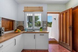 Una cocina con armarios blancos, encimera de madera, ventana con vistas y puerta al exterior.