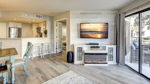 A modern kitchen with a built-in refrigerator, a dining area with a wooden table and blue chairs, a fireplace, and a large window offering a view of the outdoors. - 3123 Villamare:  Beautiful contemporary condo and newly updated, Oceanview (Hilton Head Island)