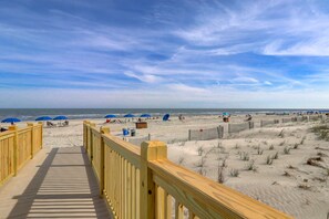 Une promenade en bois mène à une plage de sable où l’on trouve des parasols et des chaises de plage.
