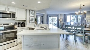 A modern kitchen with stainless steel appliances, a large island, and a dining area with a chandelier. - 3123 Villamare:  Beautiful contemporary condo and newly updated, Oceanview (Hilton Head Island)