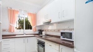 Cocina con armarios blancos, microondas, horno y lavavajillas.