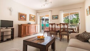Una sala de estar con una mesa de centro de madera, un sofá, un televisor, un mueble de madera y un comedor con sillas y una mesa.