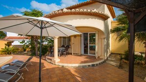 Un patio con sillones de sol, una mesa y una sombrilla grande.