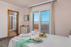 Quarto de hotel com varanda, cama com toalhas, mesa de cabeceira com frutas e bebida, e banheiro com vaso sanitário e chuveiro.