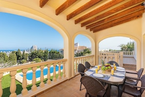 Um terraço com piscina, mesa de jantar, cadeiras e vista para o mar.