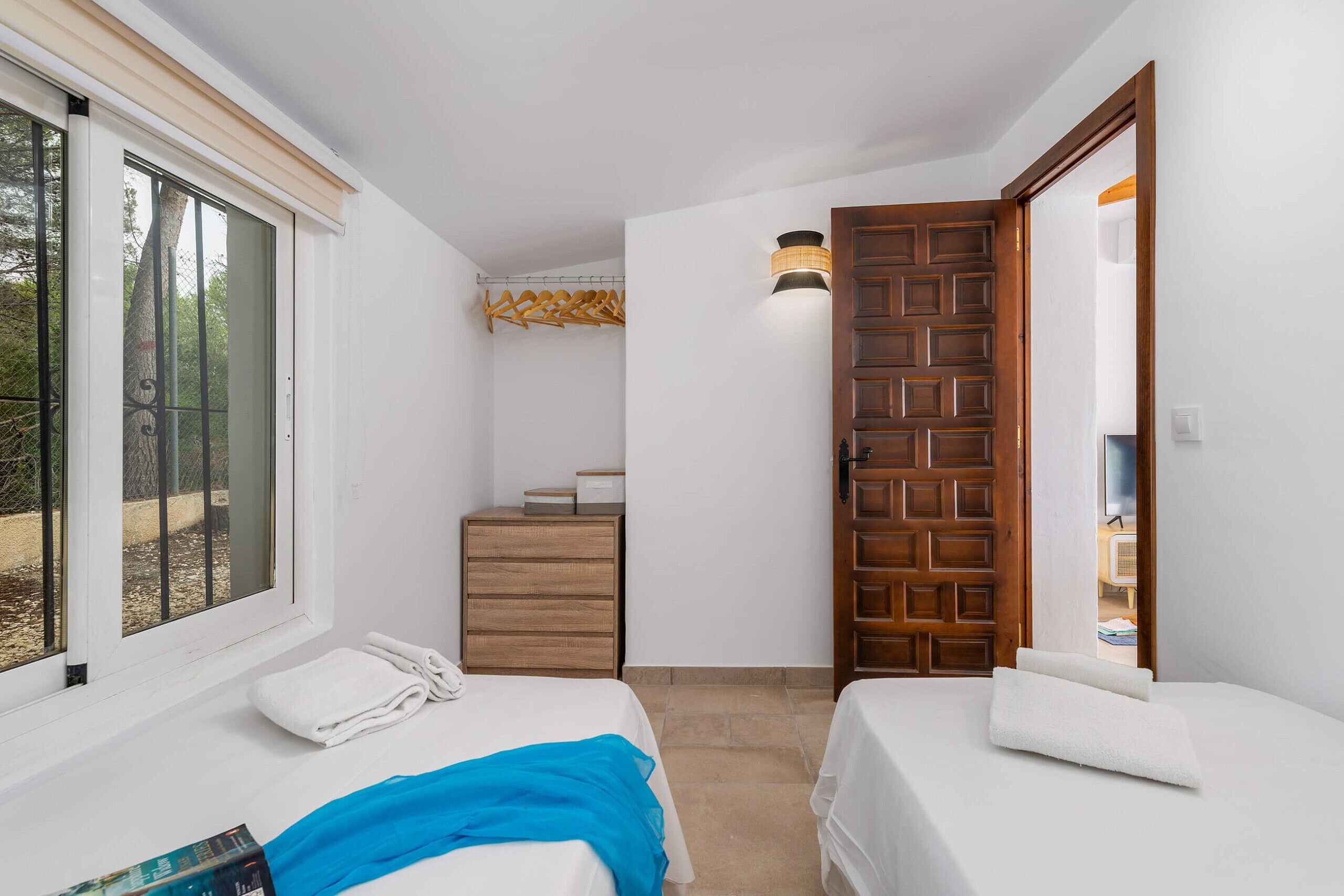 A room with two beds, a wooden dresser, a hanging coat rack, and a wooden door.