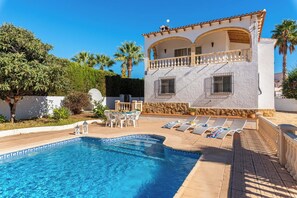 A two-story building with a pool, outdoor seating, and palm trees.