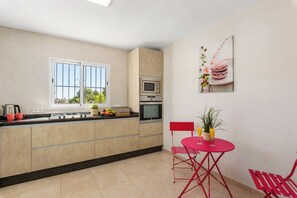 A modern kitchen with a window, a dining area with red chairs, and a wall-mounted picture.