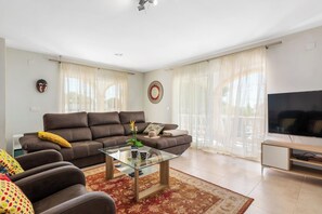 A modern living room with a brown leather sofa, a glass coffee table, and a flat-screen TV.
