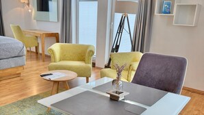 Moderni hotellihuone, jossa on sohva, nojatuoleja, pieni pöytä ja lamppu.